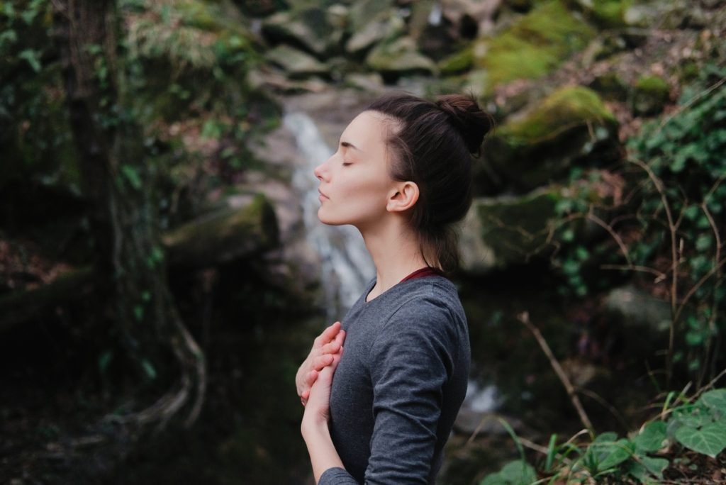 oxigenarea creierului prin meditatie - o femeie care inspira aer curat aflata in natura si tinand mainile pe piept
