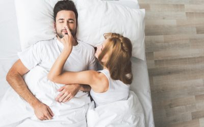 Happy married couple awaking together in the morning Wake up, my darling. Top view of cheerful young woman touching nose of her sleeping husband. Man is lying on bed with closed eyes