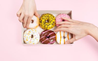 Hands is taking colored glazed donuts in donut box. Hands is grabbing different flavors doughnuts. Unhealthy snack in the office or a break office. Hands is taking colored glazed donuts in donut box. Hands is grabbing different flavors doughnuts. Unhealthy snack in the office or a break office. Copy space, mock up